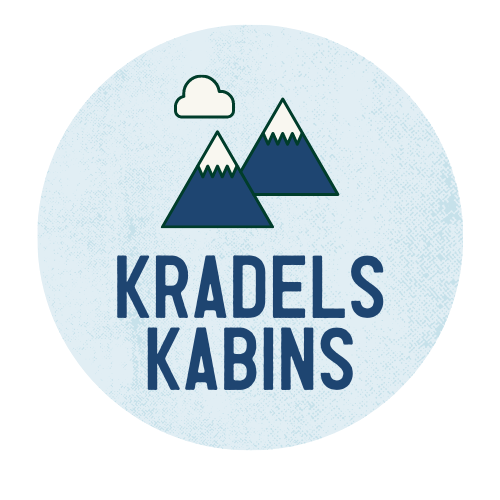 Round logo with a light blue textured background with the outlines of two mountains and a cloud in the foreground in dark blue. Underneath is "Kradels Kabins" in an all-caps font and a dark blue color