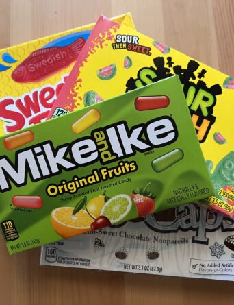 A selection of candy boxes stacked on top of each other. Mike & Ike is on the top, and you can see a bit of the Sour Patch box and Swedish Fish box underneath. On the bottom is a Snowcaps box that is mostly hidden by the other boxes