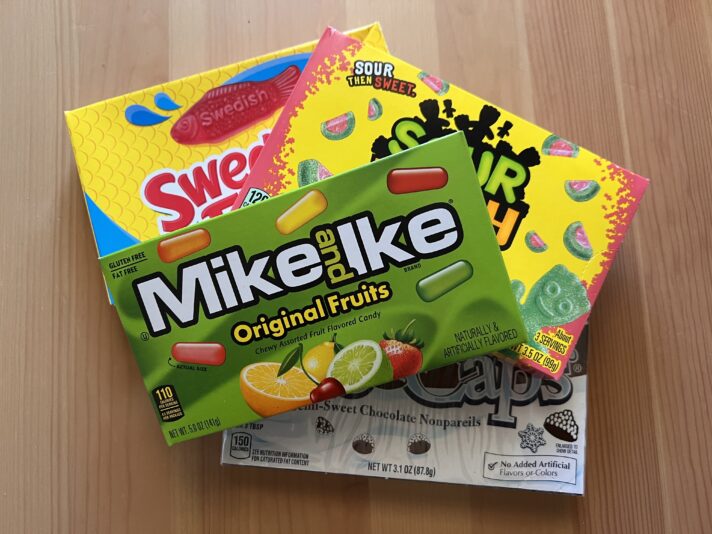 A selection of candy boxes stacked on top of each other. Mike & Ike is on the top, and you can see a bit of the Sour Patch box and Swedish Fish box underneath. On the bottom is a Snowcaps box that is mostly hidden by the other boxes